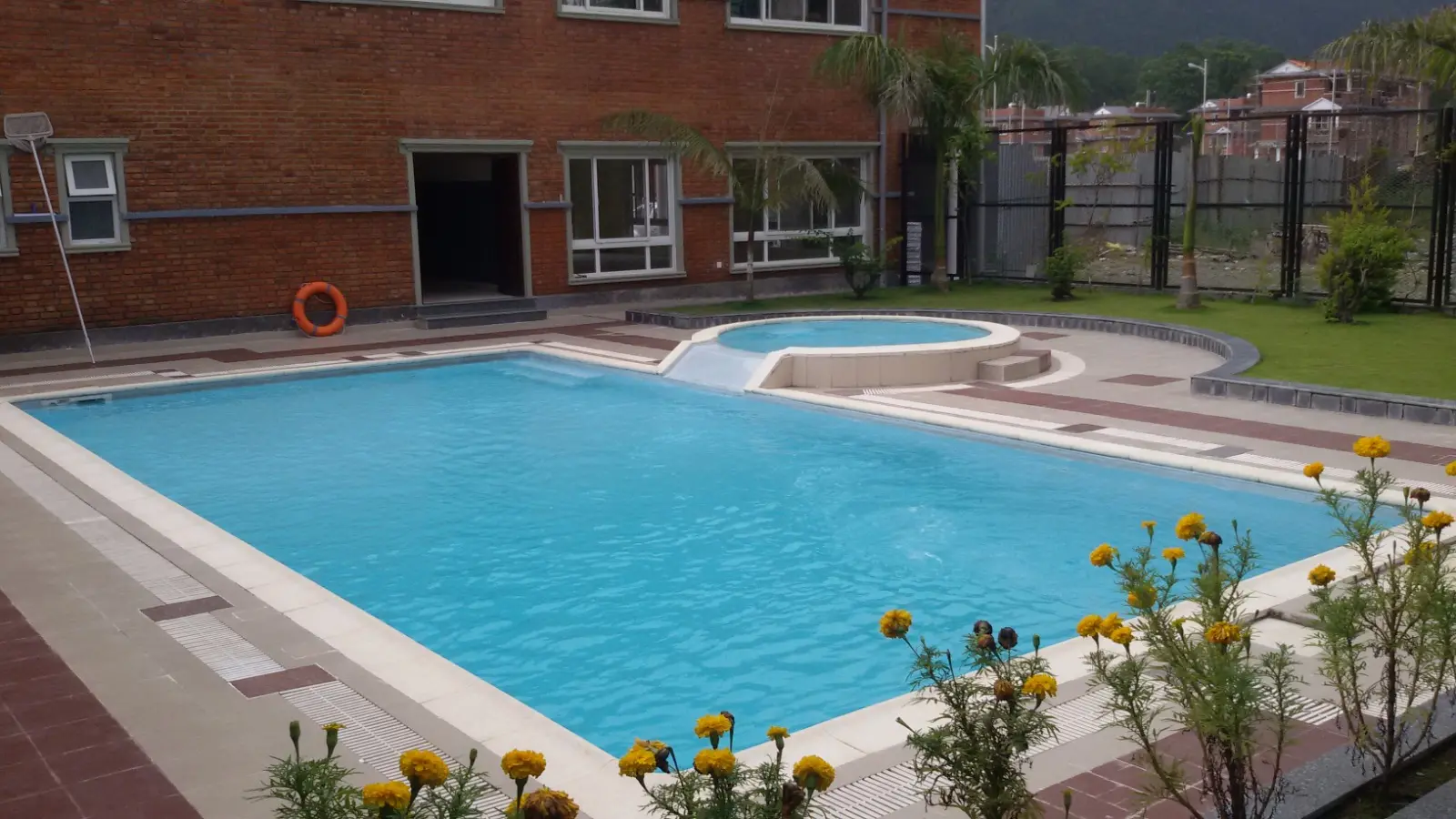 Pool construction stage 6: the completed swimming pool and adjoining round pool filled with water, beside a paved deck and marigolds.